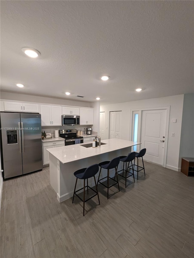 kitchen with a center island with sink, a kitchen breakfast bar, wood finished floors, stainless steel appliances, and a sink