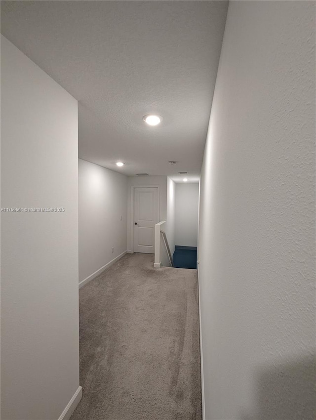 hall featuring baseboards, carpet flooring, a textured ceiling, and an upstairs landing