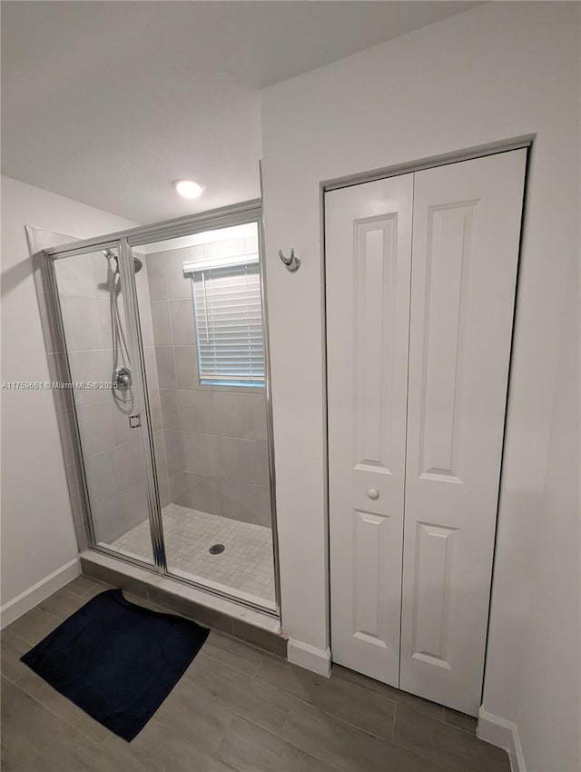 full bath featuring wood finish floors, a shower stall, and baseboards