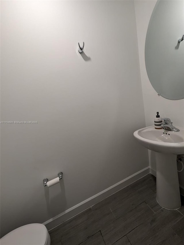 bathroom featuring toilet, a sink, baseboards, and wood finished floors