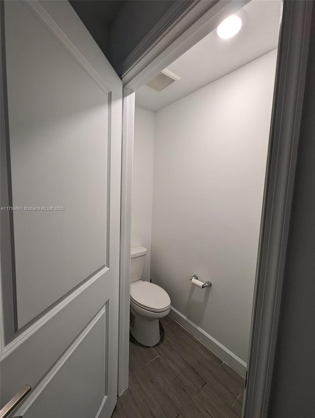 bathroom with baseboards, visible vents, toilet, and wood finished floors