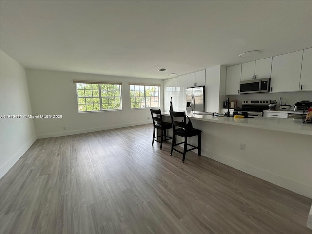 kitchen featuring wood finished floors, baseboards, open floor plan, light countertops, and appliances with stainless steel finishes