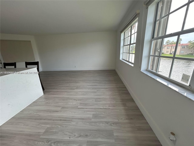 empty room with a water view, light wood-style flooring, and baseboards