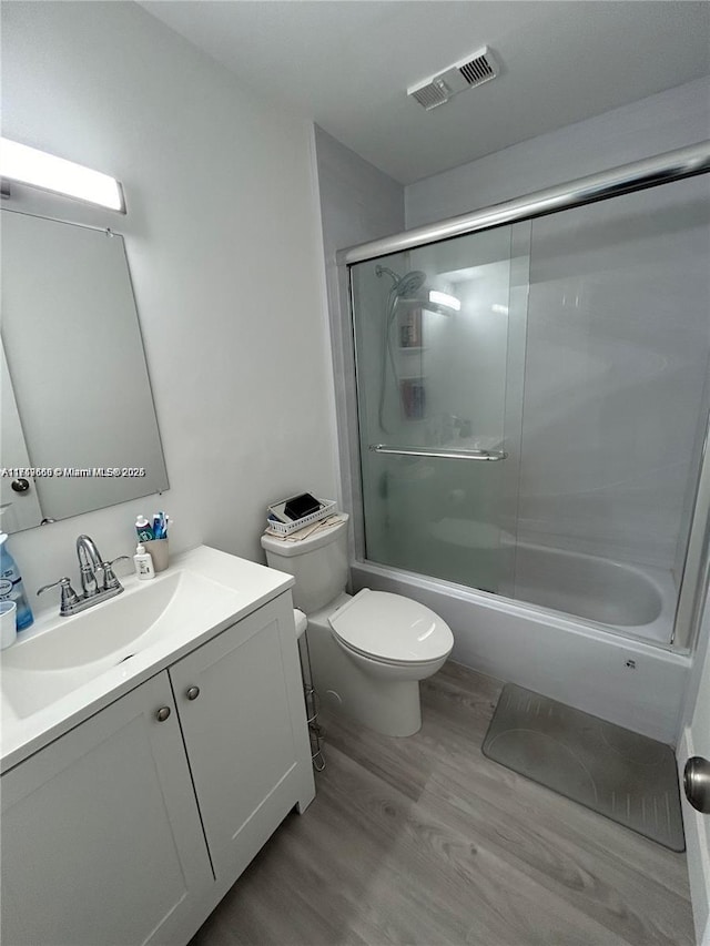 bathroom with bath / shower combo with glass door, visible vents, toilet, vanity, and wood finished floors