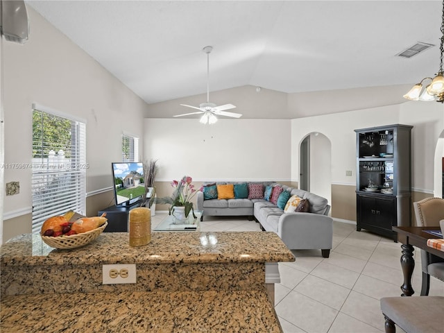 living room with arched walkways, light tile patterned floors, visible vents, ceiling fan, and vaulted ceiling