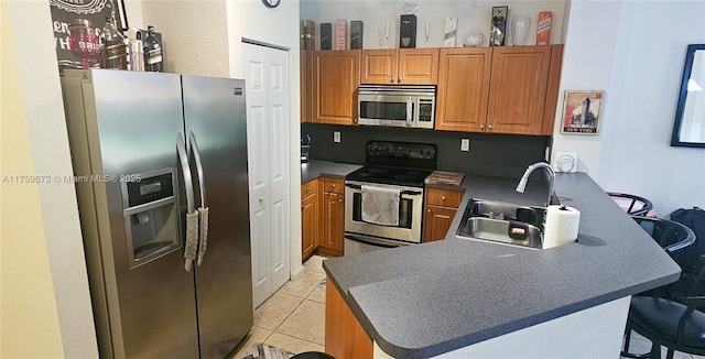 kitchen featuring brown cabinetry, appliances with stainless steel finishes, a peninsula, a sink, and light tile patterned flooring