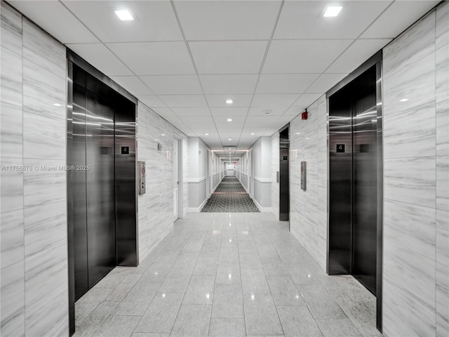 corridor with elevator, a drop ceiling, tile walls, and tile patterned floors