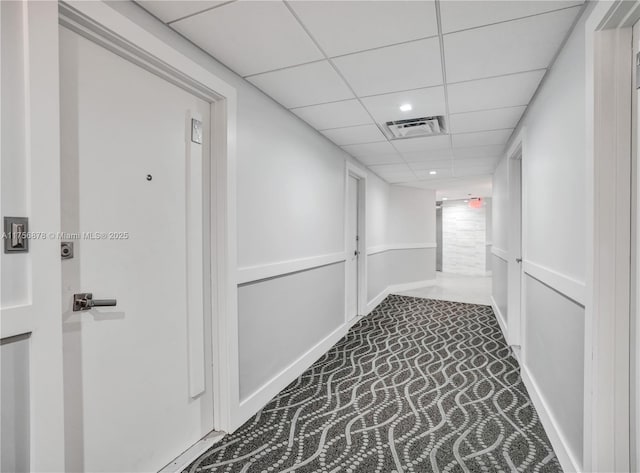 hallway featuring baseboards, carpet, visible vents, and a drop ceiling