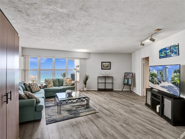 living area featuring a textured ceiling, light wood finished floors, and baseboards