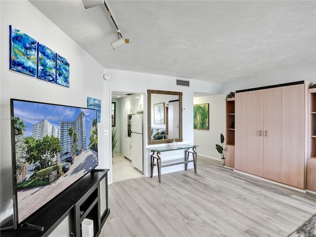 interior space featuring visible vents, ensuite bath, freestanding refrigerator, light wood-style floors, and track lighting