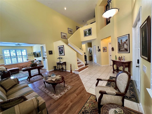 living area featuring light wood-type flooring, stairway, baseboards, and a towering ceiling