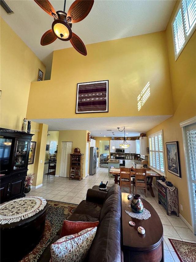 living area with visible vents, baseboards, light tile patterned floors, a high ceiling, and a ceiling fan