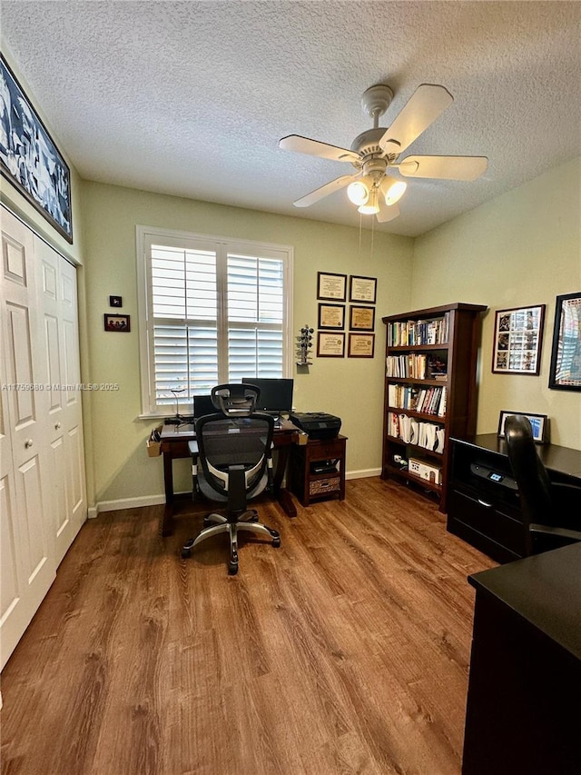 home office featuring a ceiling fan, wood finished floors, baseboards, and a textured ceiling