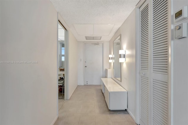 hallway featuring attic access, light tile patterned flooring, a textured ceiling, and baseboards