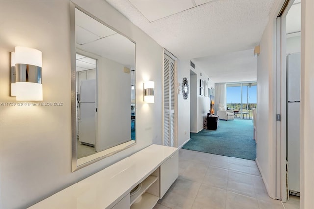 hall with a textured ceiling, light tile patterned flooring, light carpet, baseboards, and a wall of windows