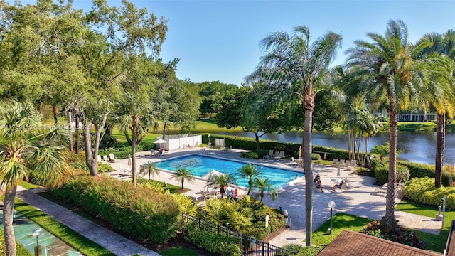 community pool with a water view, a patio area, and fence