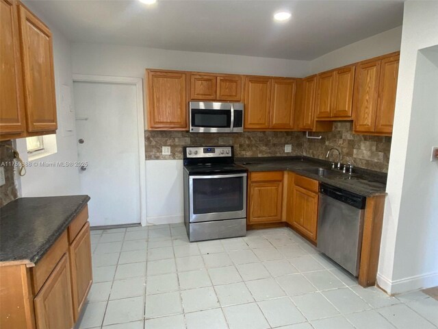 kitchen with a sink, decorative backsplash, dark countertops, and appliances with stainless steel finishes