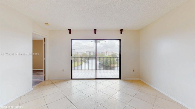 unfurnished room with a textured ceiling, light tile patterned flooring, and baseboards