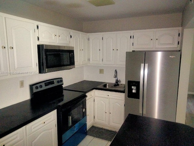 kitchen with stainless steel refrigerator with ice dispenser, dark countertops, black range with electric stovetop, white cabinetry, and a sink