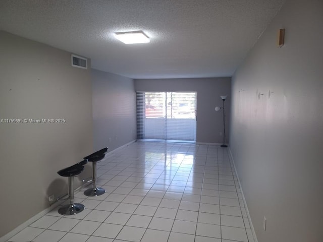 unfurnished room featuring light tile patterned floors, baseboards, visible vents, and a textured ceiling