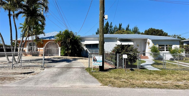 view of front facade with metal roof, driveway, a fenced front yard, and a gate