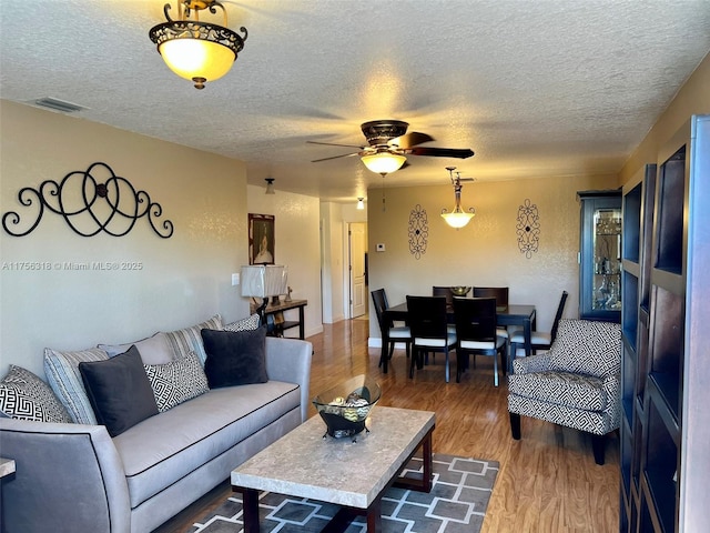 living room featuring a textured ceiling, ceiling fan, wood finished floors, and visible vents