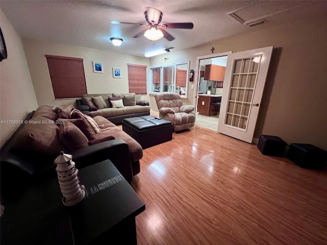 living area with light wood-style floors, a textured ceiling, visible vents, and a ceiling fan