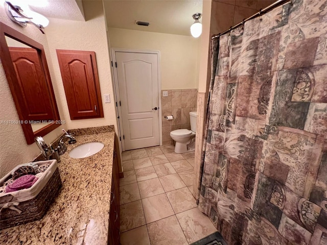 bathroom with toilet, a shower with shower curtain, vanity, visible vents, and tile walls