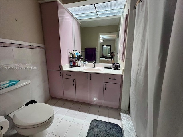 ensuite bathroom featuring tile walls, curtained shower, toilet, vanity, and tile patterned flooring