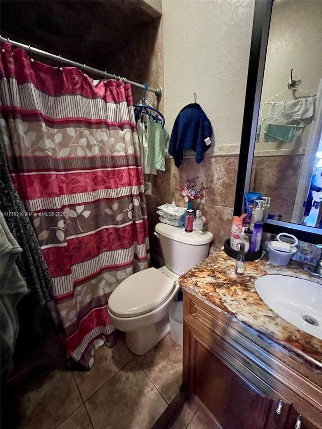 bathroom featuring wainscoting, toilet, tile patterned floors, vanity, and tile walls