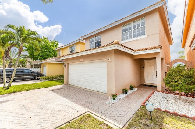 mediterranean / spanish-style house with a garage, decorative driveway, a tiled roof, and stucco siding