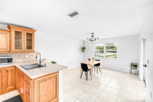 kitchen featuring tasteful backsplash, stainless steel microwave, visible vents, a sink, and a peninsula