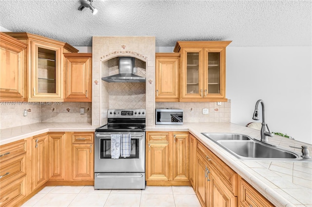 kitchen with light tile patterned floors, wall chimney exhaust hood, stainless steel appliances, light countertops, and a sink