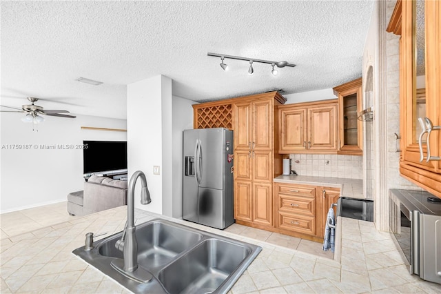 kitchen with a sink, a ceiling fan, brown cabinets, tasteful backsplash, and stainless steel fridge