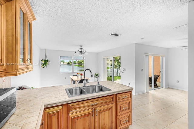 kitchen featuring visible vents, tile countertops, glass insert cabinets, brown cabinets, and a sink