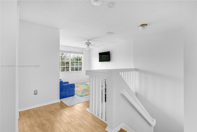 corridor with baseboards, light wood finished floors, an upstairs landing, and a textured ceiling