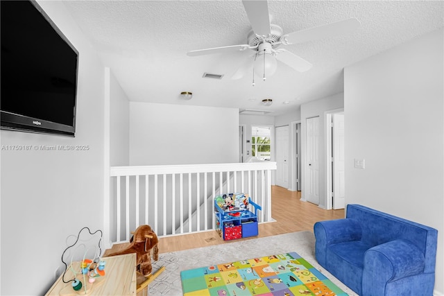 game room with a ceiling fan, visible vents, a textured ceiling, and wood finished floors