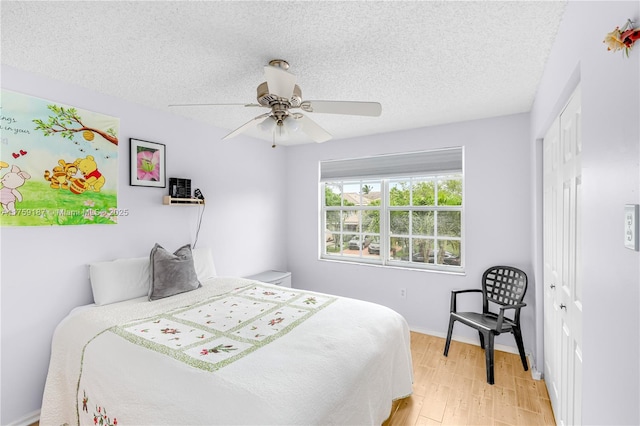 bedroom with a closet, light wood-style flooring, ceiling fan, a textured ceiling, and baseboards