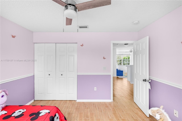 unfurnished bedroom featuring a closet, visible vents, light wood-style flooring, ceiling fan, and a textured ceiling