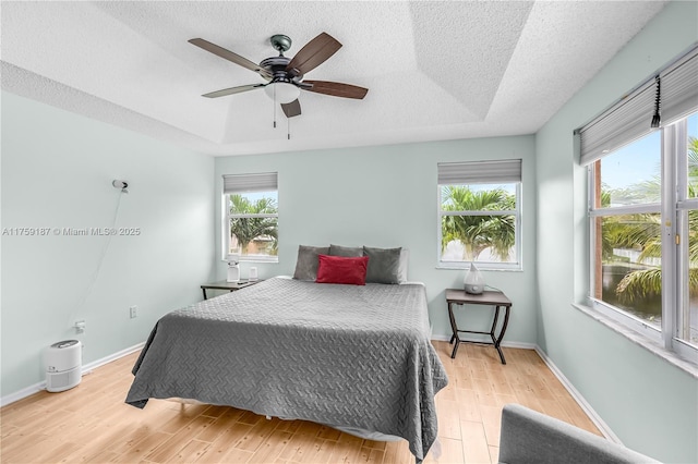 bedroom featuring light wood finished floors, multiple windows, and a raised ceiling