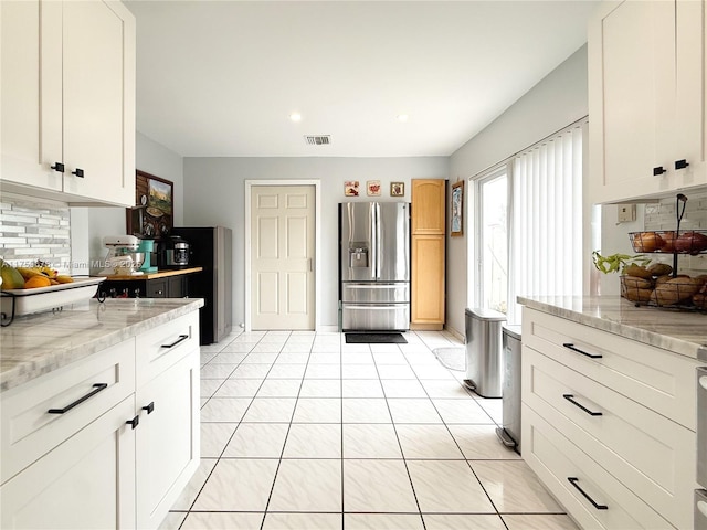 kitchen featuring backsplash, light stone countertops, stainless steel refrigerator with ice dispenser, light tile patterned flooring, and white cabinets