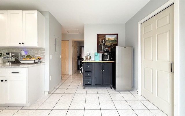 kitchen with white cabinetry, light countertops, backsplash, and freestanding refrigerator