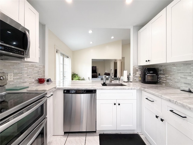 kitchen with tasteful backsplash, vaulted ceiling, appliances with stainless steel finishes, white cabinets, and a sink