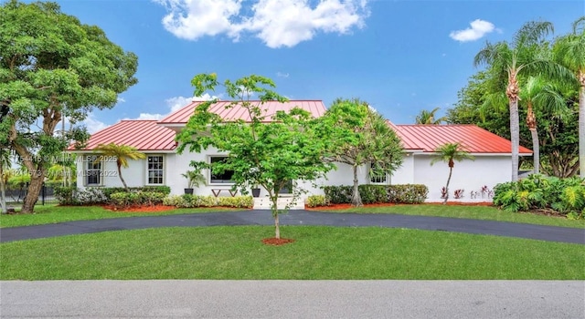 view of front facade with aphalt driveway, stucco siding, a standing seam roof, metal roof, and a front lawn