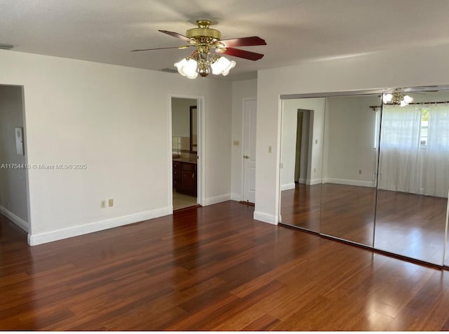 unfurnished bedroom featuring baseboards, ensuite bath, wood finished floors, a closet, and ceiling fan with notable chandelier