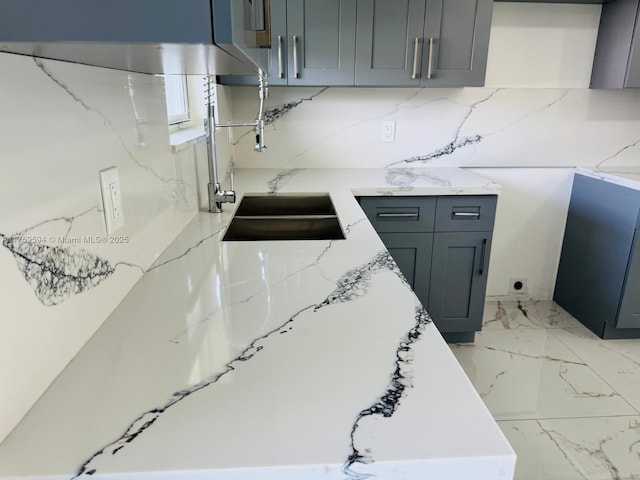 kitchen with marble finish floor, gray cabinetry, a sink, decorative backsplash, and light stone countertops