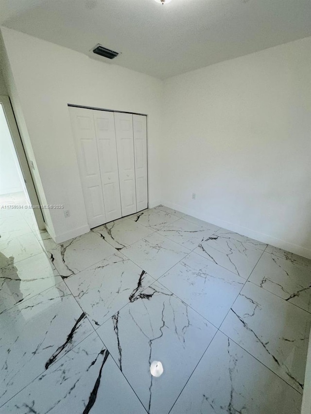 unfurnished bedroom featuring a closet, visible vents, marble finish floor, and baseboards