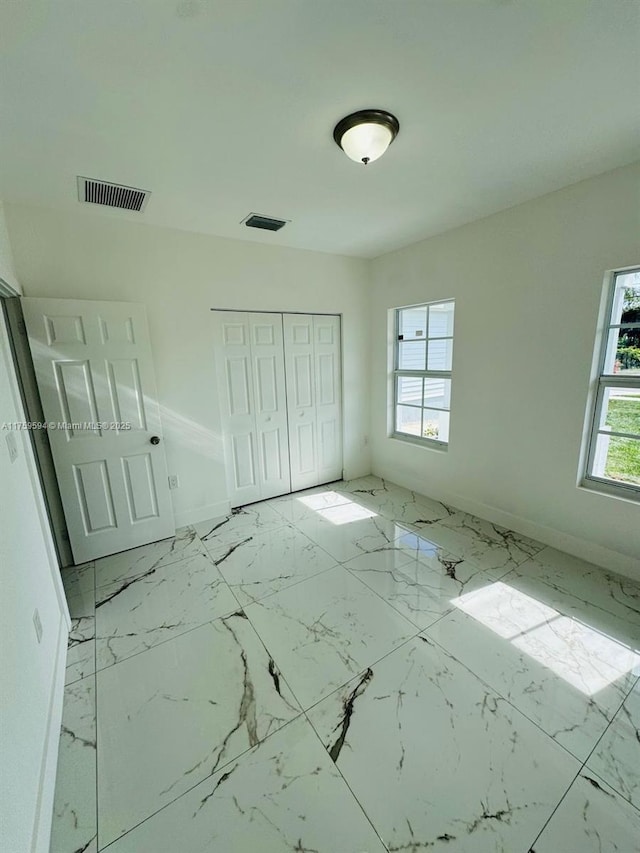 unfurnished bedroom featuring a closet, visible vents, marble finish floor, and baseboards