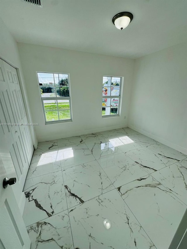 interior space featuring a closet, multiple windows, marble finish floor, and baseboards