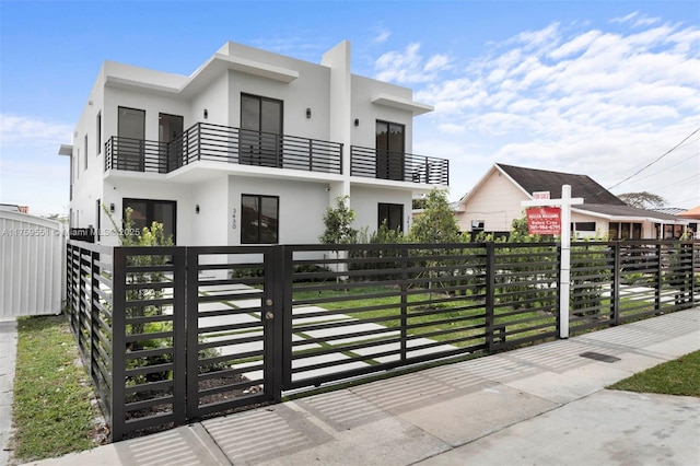 view of front facade with a fenced front yard, a gate, a balcony, and stucco siding